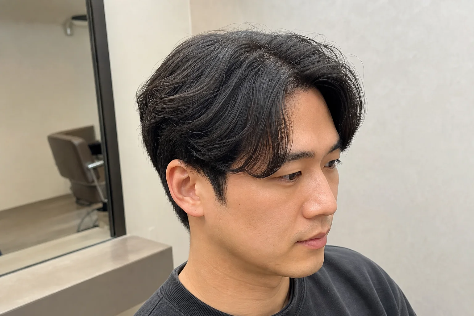 男士中分的侧前方细节，展示柔和分线、脸侧落点、顶部支撑和耳上重量